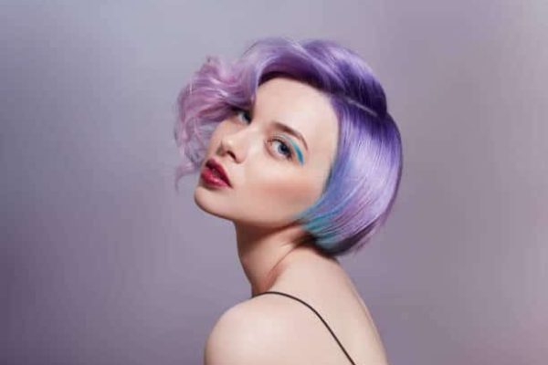 Portrait of a woman with bright colored flying hair, all shades of purple. Hair coloring, beautiful lips and makeup. Hair fluttering in the wind. Sexy girl with short  hair. Professional coloring